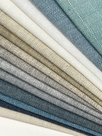 A collection of fabric swatches in various shades of beige, gray, and blue. The swatches are arranged in a fan shape, with the lightest colors at the top and the darkest colors at the bottom. The fabric has a textured, woven appearance.