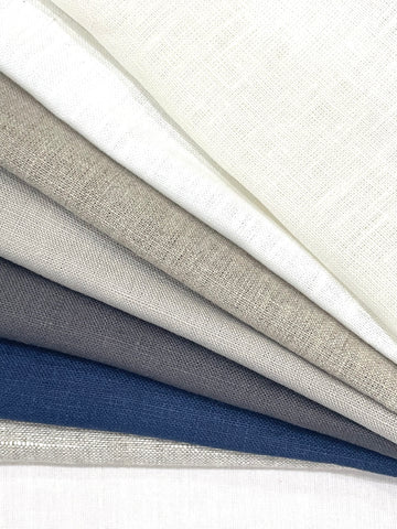 Stack of folded 100% natural linen fabric in multiple earthy colors, 118-inch double width.