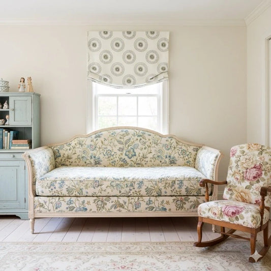 round linen relaxed casual roman shade, floral patterned sofa and chair in a room with a window and bookshelf.
