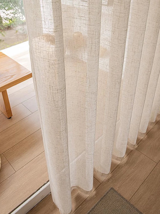 Sheer white curtain in a room with wooden flooring and a table.