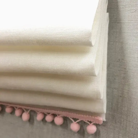 Folded fabric with pink pom-pom trim on a neutral background