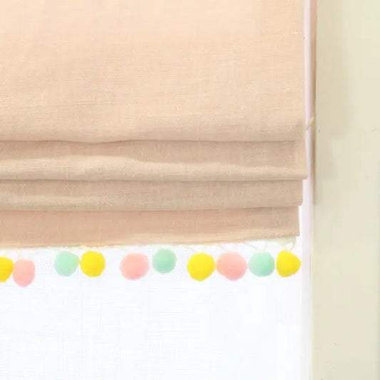 Beige roman shade with a colorful pom-pom garland at the bottom