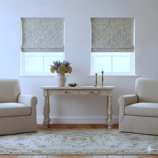 Living room with damask linen roman shade, beige armchairs, a small table with decor items, and patterned roman blinds.