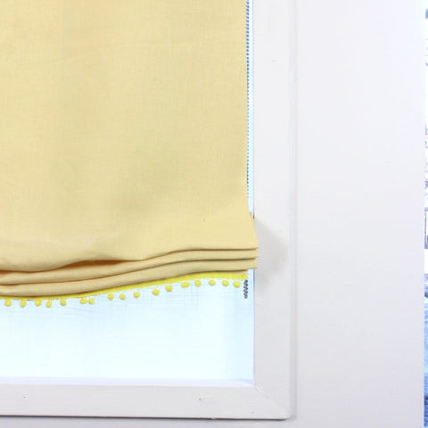 Yellow linen relaxed Roman shade featuring soft yellow pom pom trim, ideal for nursery or kids' room decor with optional blackout lining.