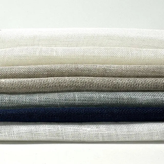Folded stack of sheer linen fabric in seven natural colors