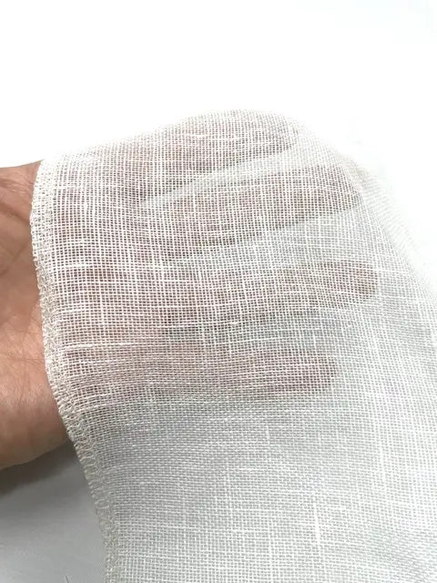 Hand holding white sheer linen fabric showing its airy transparency