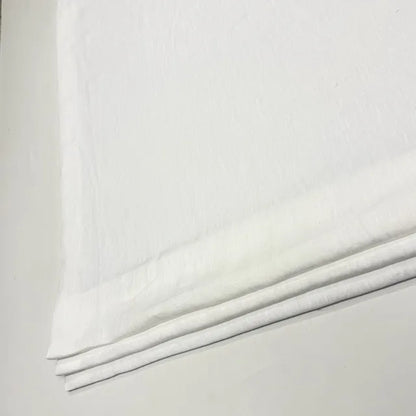 A close-up of folded white linen fabric, likely cotton or linen, showing its soft texture and layered edges against a light neutral background.