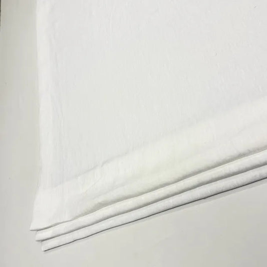 A close-up of folded white linen fabric, likely cotton or linen, showing its soft texture and layered edges against a light neutral background.
