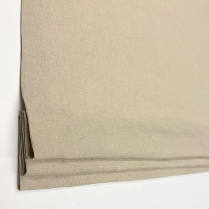A close-up of a natural linen fabric roman shade or curtain panel folded over on a plain white background.