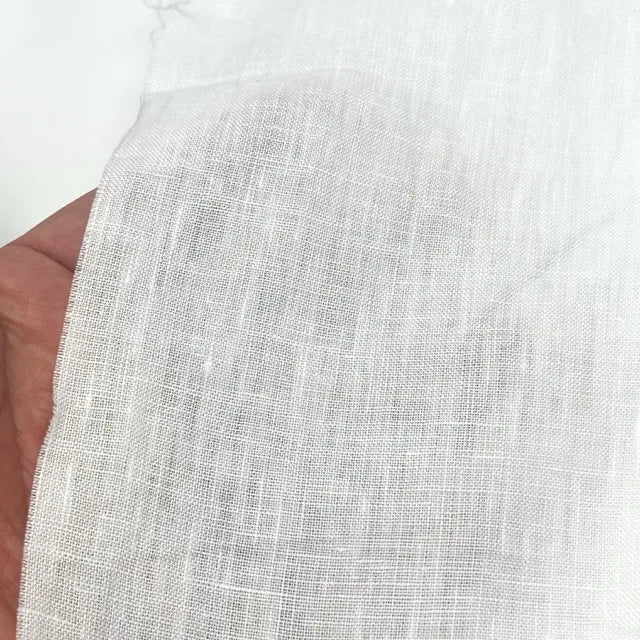 A close-up of a hand holding a piece of white textured fabric, showing its woven linen-like pattern against a plain white background.