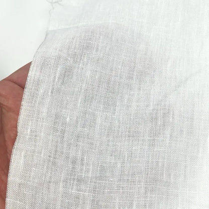 A close-up of a hand holding a piece of white textured fabric, showing its woven linen-like pattern against a plain white background.