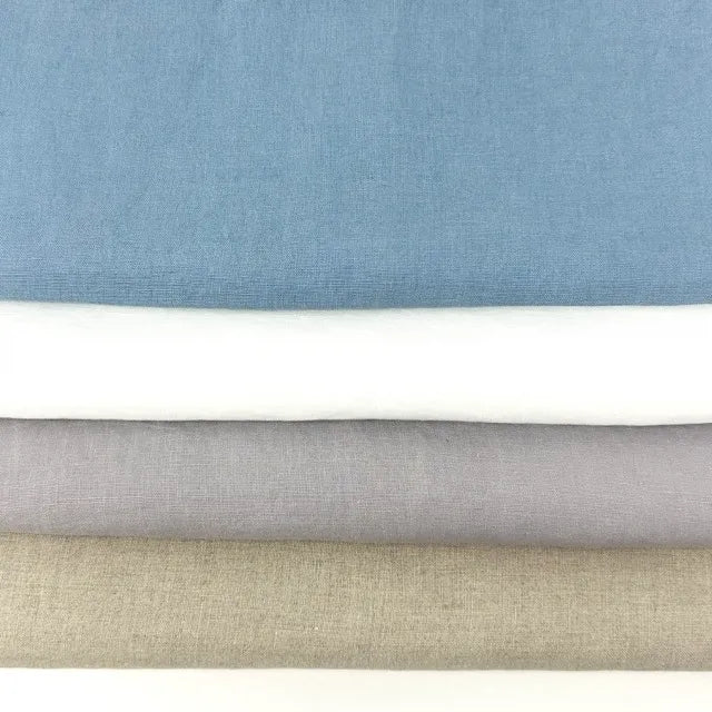 Four folded fabric swatches stacked horizontally, showing different colors: dusty blue, white, light gray, and beige, with a white surface visible at the very bottom.