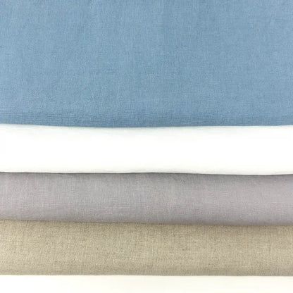 Four folded fabric swatches stacked horizontally, showing different colors: dusty blue, white, light gray, and beige, with a white surface visible at the very bottom.