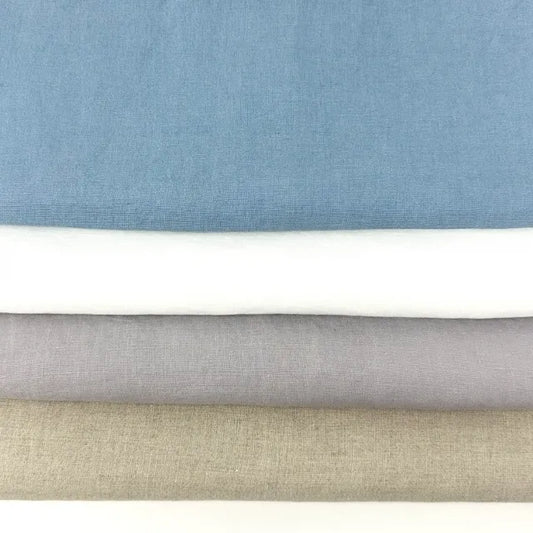 Four folded fabric swatches stacked horizontally, showing different colors: dusty blue, white, light gray, and beige, with a white surface visible at the very bottom.