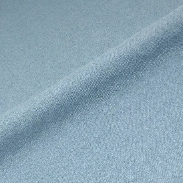 A close-up of light blue fabric with a soft diagonal fold showing the material texture.