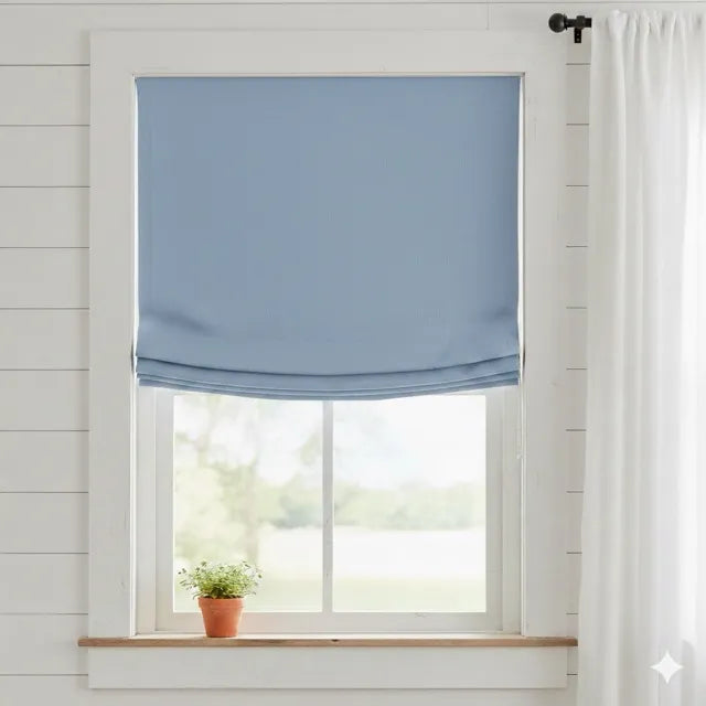A light blue french linen relaxed roman shade partially drawn on a white-framed window, set in a bright room with white shiplap walls, a small potted plant on the sill, and a white curtain to the right.