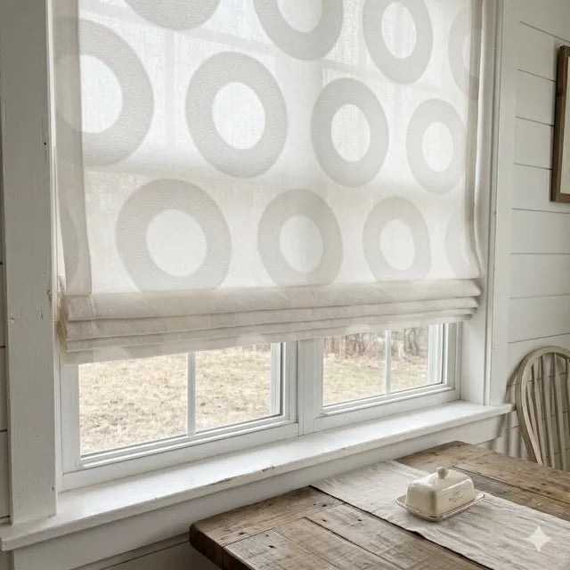 Window with a circle white roman shade in a room with wooden furniture and a chair.