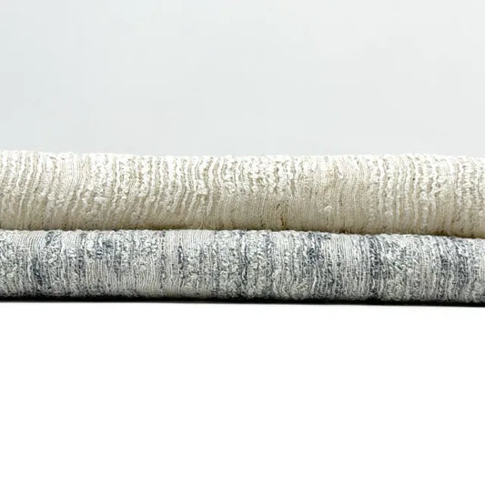 Three rolls of textured linen fabric in beige, gray, and white on a light gray background