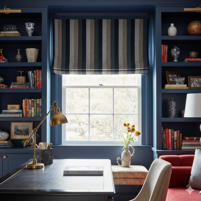 Home office with blue walls, bookshelves, a desk, and a window with striped roman shade.