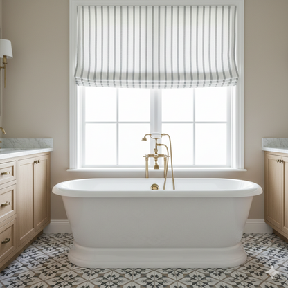White freestanding bathtub in a bathroom with a window and striped linen flat roman shade.