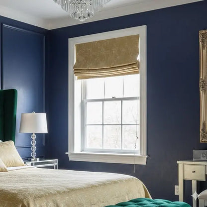 Neatly made bed in a bedroom with navy walls, a window with gold jacquard roman shade, and decorative elements.