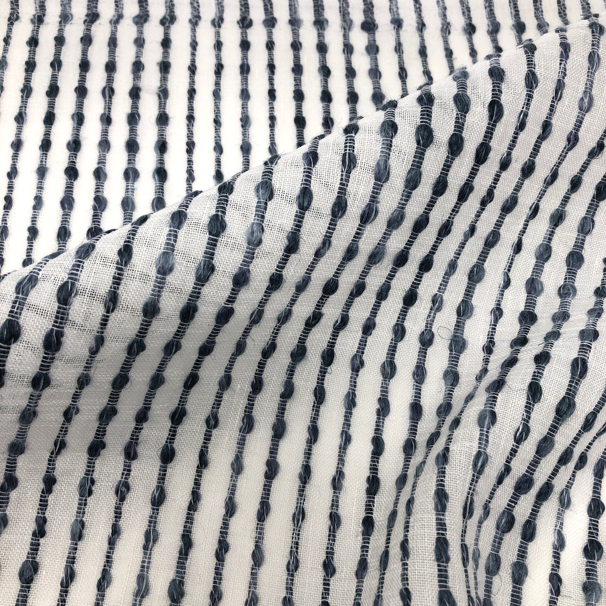 Close-up of sheer linen fabric with dark vertical embroidered stripes on a white background, style CL1032.