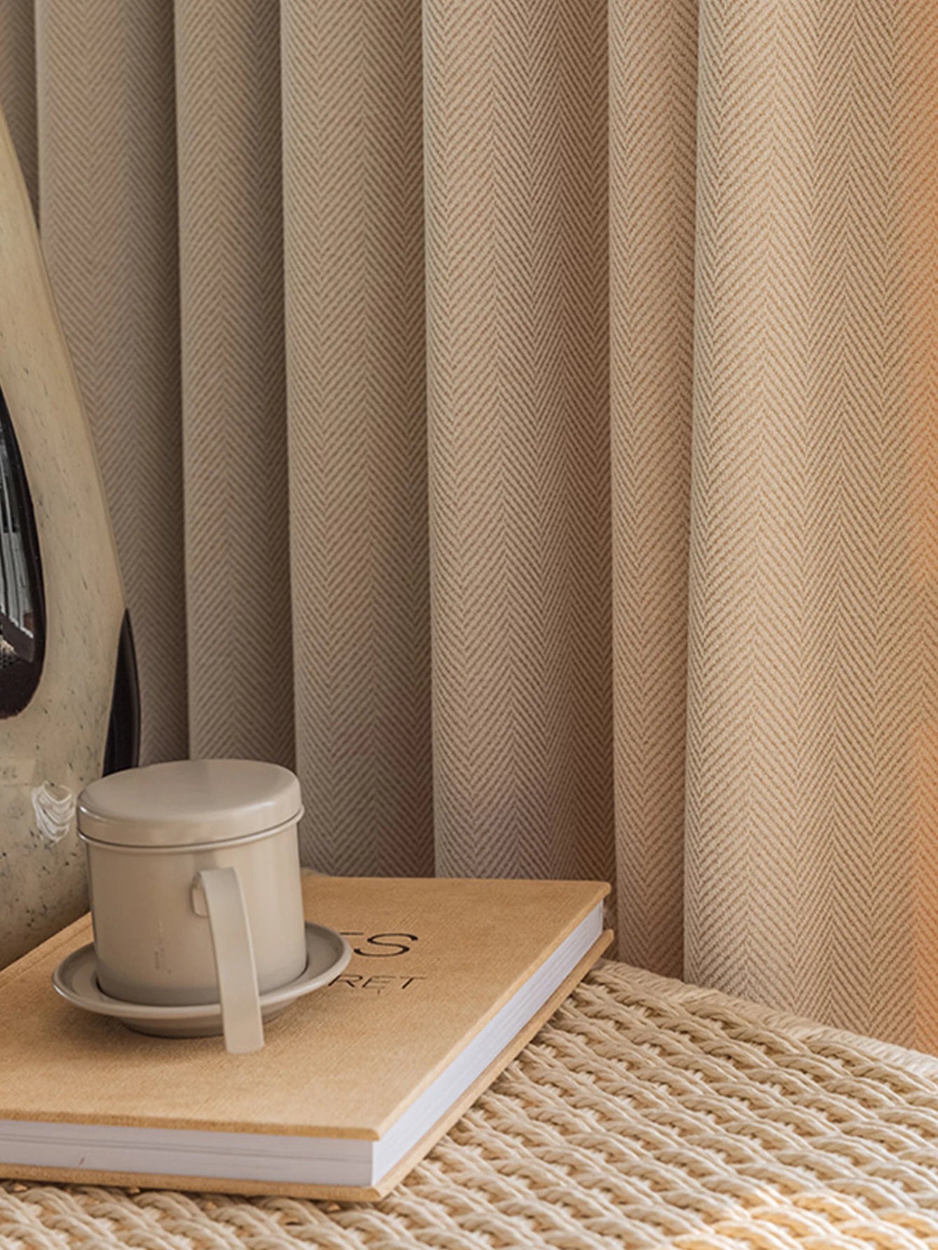 Curtains with a woven texture, a cup on a notebook, and a textured surface.