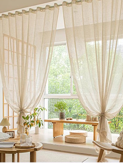 Sheer white curtains in a bright room with a wooden table and plants.