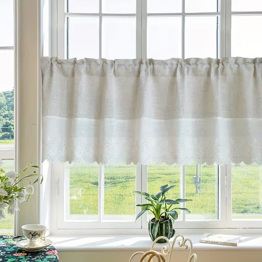 A white tierce curtain with a gathered top and scalloped eyelet hem hanging on a window in a bright room, with a green field visible outside.