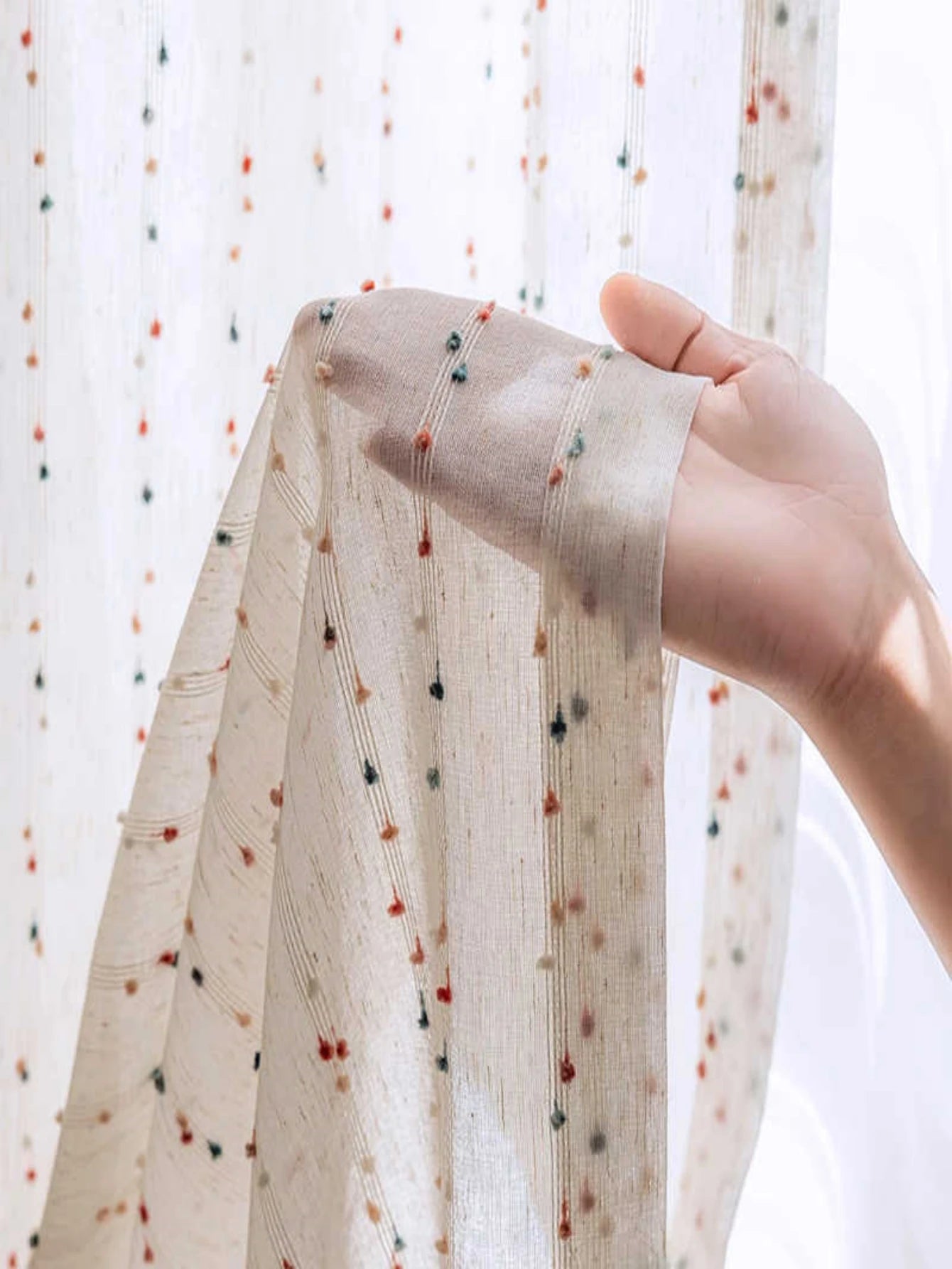 Hand holding a piece of fabric with small colorful dots against a light background