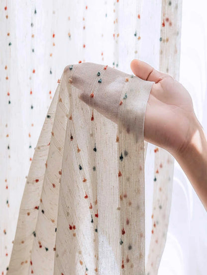 Hand holding a piece of fabric with small colorful dots against a light background