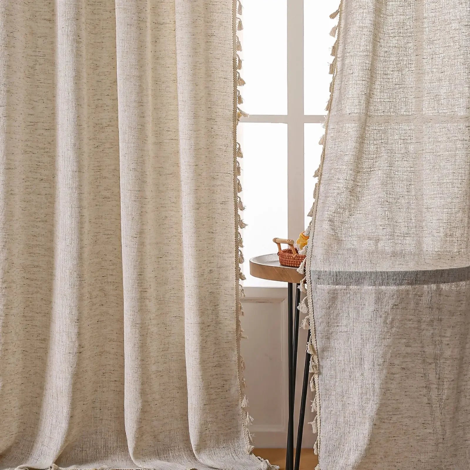Textured beige curtains with tassels in a room with a small table and decor items.