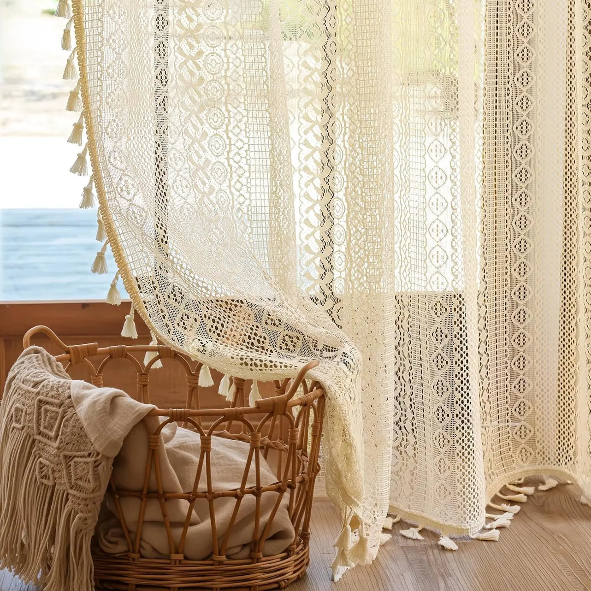 Lace curtain with tassels in a room with a wicker chair and blanket.