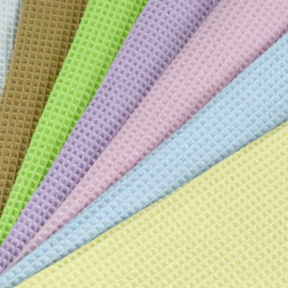 A close-up fan arrangement of textured waffle-weave fabric in multiple pastel and earthy colors, including white, tan, lime green, lavender, pink, light blue, and pale yellow.