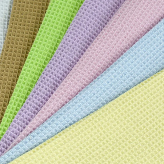 A close-up fan arrangement of textured waffle-weave fabric in multiple pastel and earthy colors, including white, tan, lime green, lavender, pink, light blue, and pale yellow.
