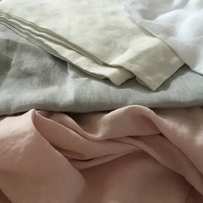 Stack of folded fabric sheets in various colors including beige, white, and pink.