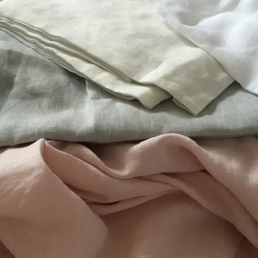 Stack of folded fabric sheets in various colors including beige, white, and pink.