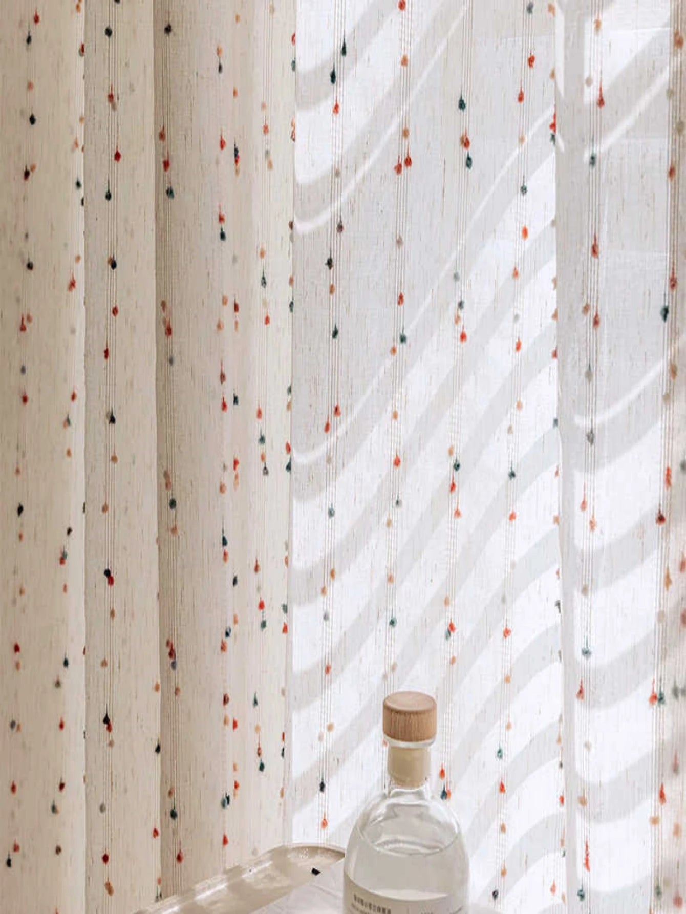 Glass bottle with a wooden cap against a patterned curtain