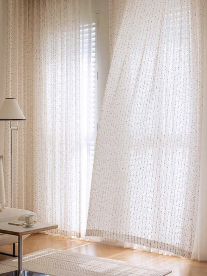 Sheer white curtains in a room with a lamp and table.