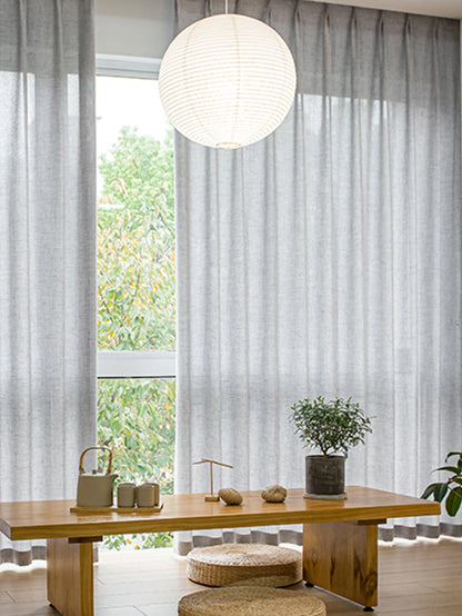 Modern interior with light gray curtains, a wooden table, and a spherical pendant light.