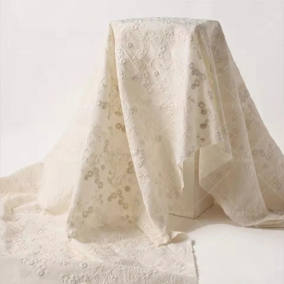 An ivory lace fabric with delicate floral embroidery draped over a white block against a clean white background.