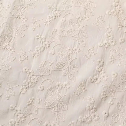 Close-up of a cream-colored fabric with delicate floral embroidery and embroidered leaf patterns.