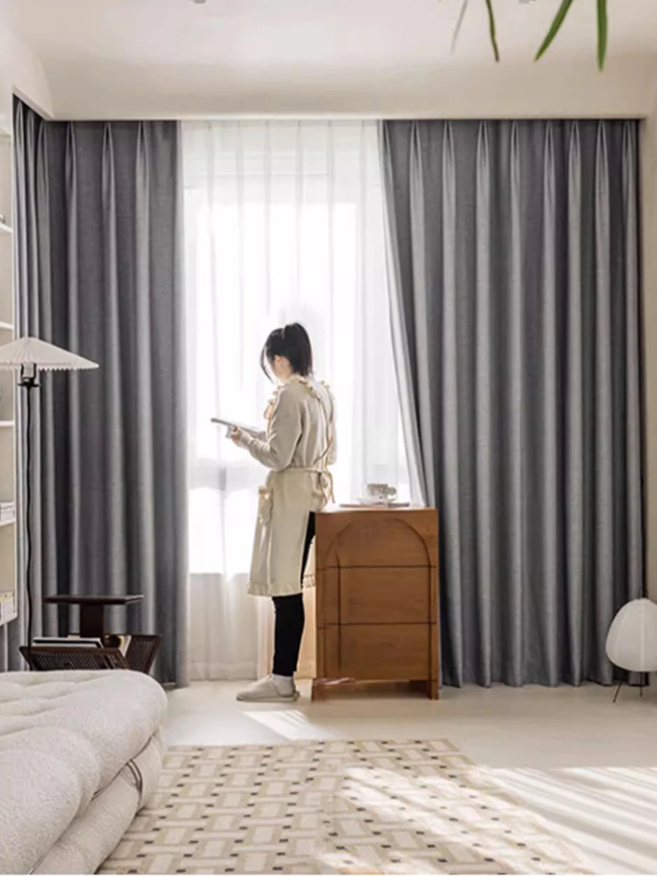 Person standing in a room with gray curtains and a wooden dresser.