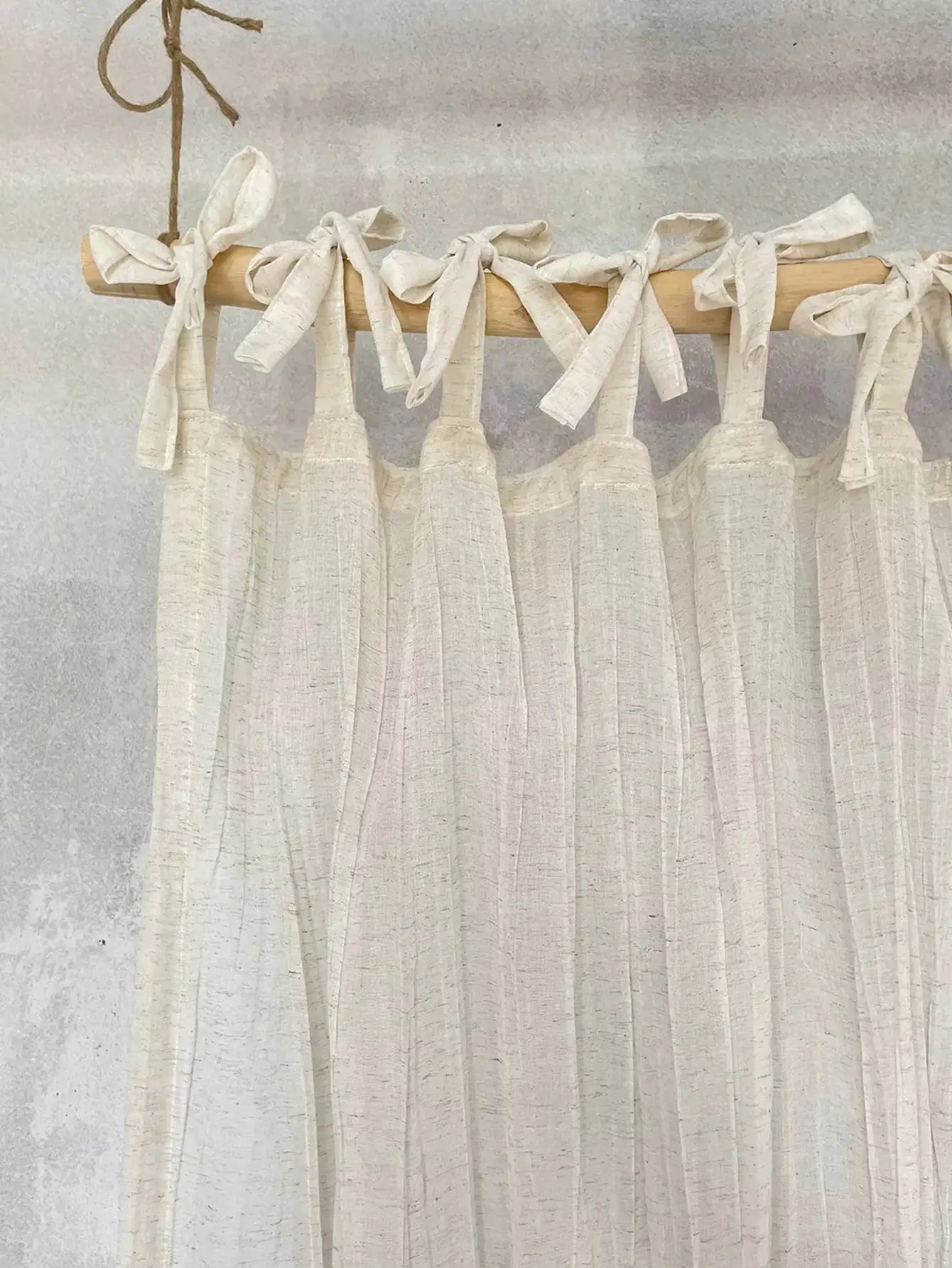 Sheer white curtain with wooden rod and tied ribbons against a neutral background