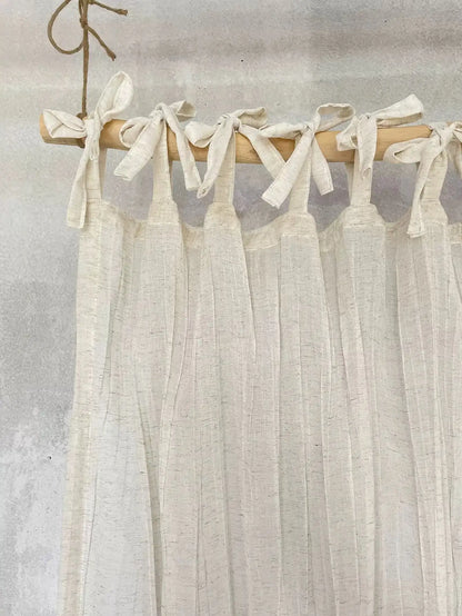 Sheer white curtain with wooden rod and tied ribbons against a neutral background
