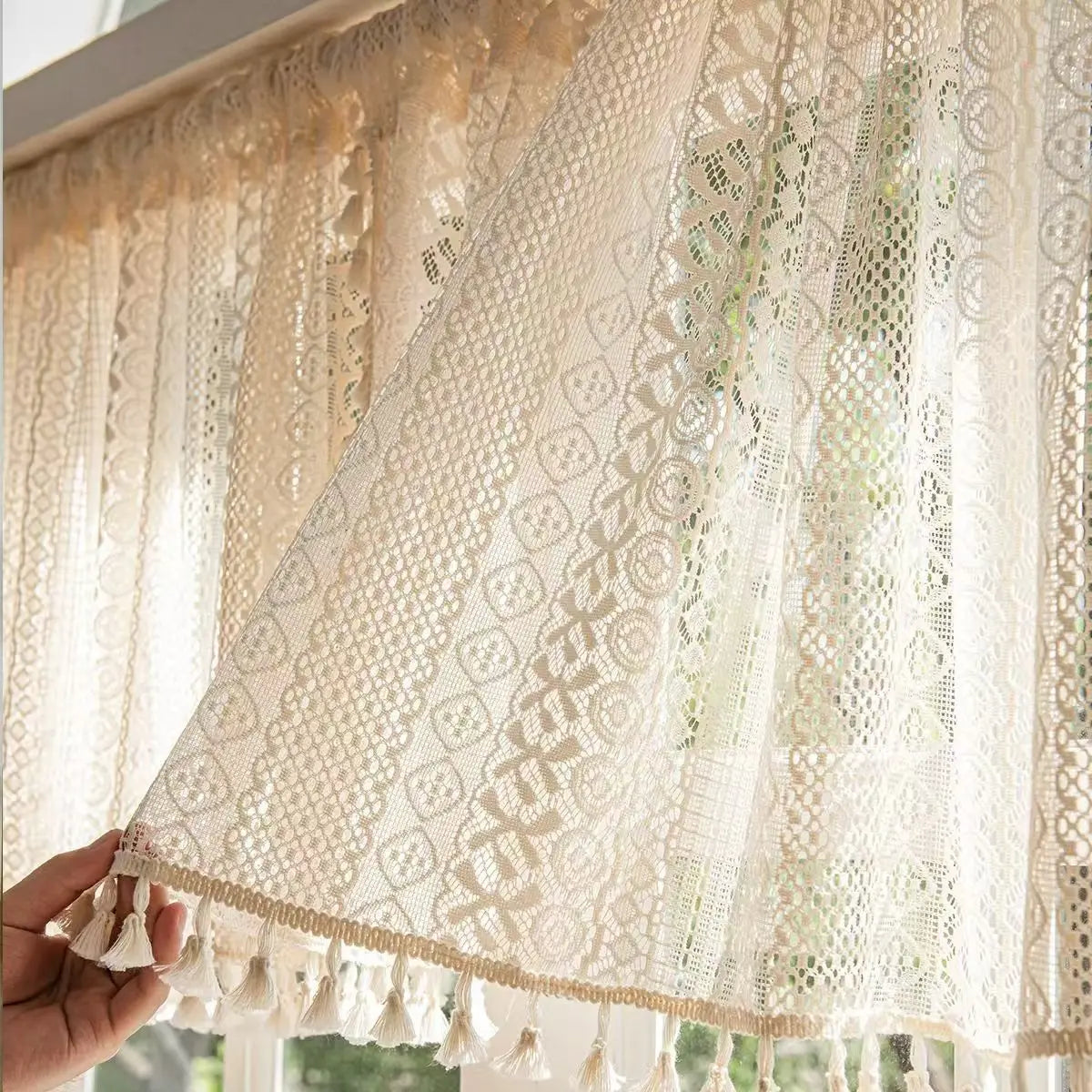 Lace curtain with tassels held by a hand, with a blurred indoor background