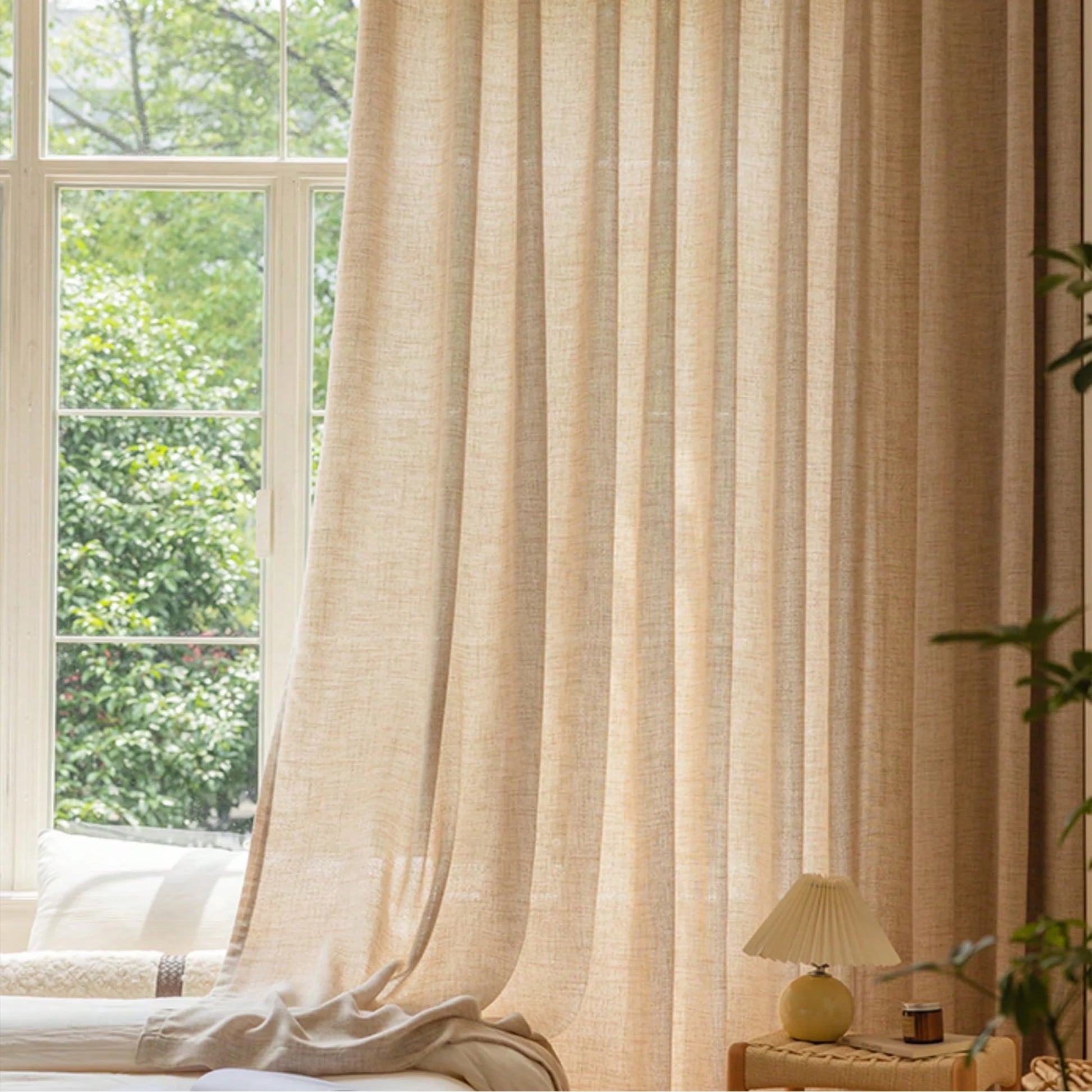 Beige curtain in a room with a window showing greenery outside.