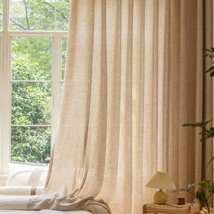 Beige curtain in a room with a window showing greenery outside.