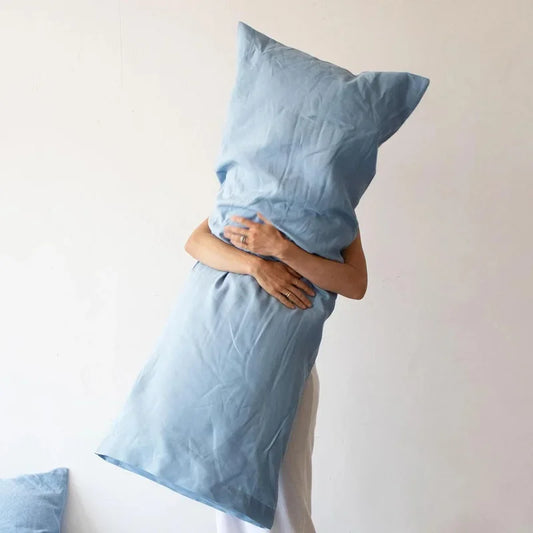 Person wrapped in a blue satin sheet with a pillow on a plain background