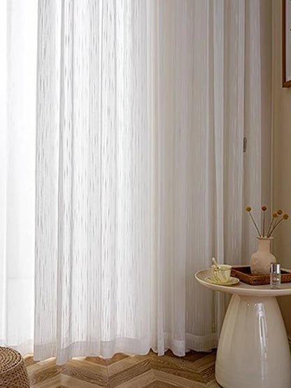Sheer white curtain in a room with a small table and decor items.
